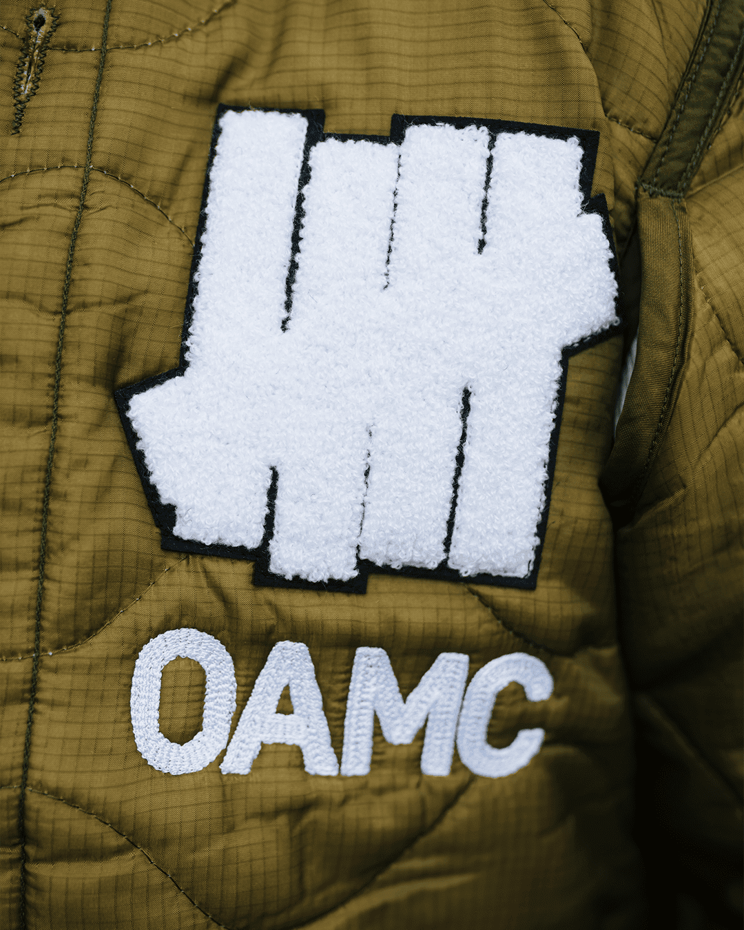 UNDEFEATED 與 OAMC 首度攜手合作，推出一款致敬雙方運動與軍事血統的外套。1